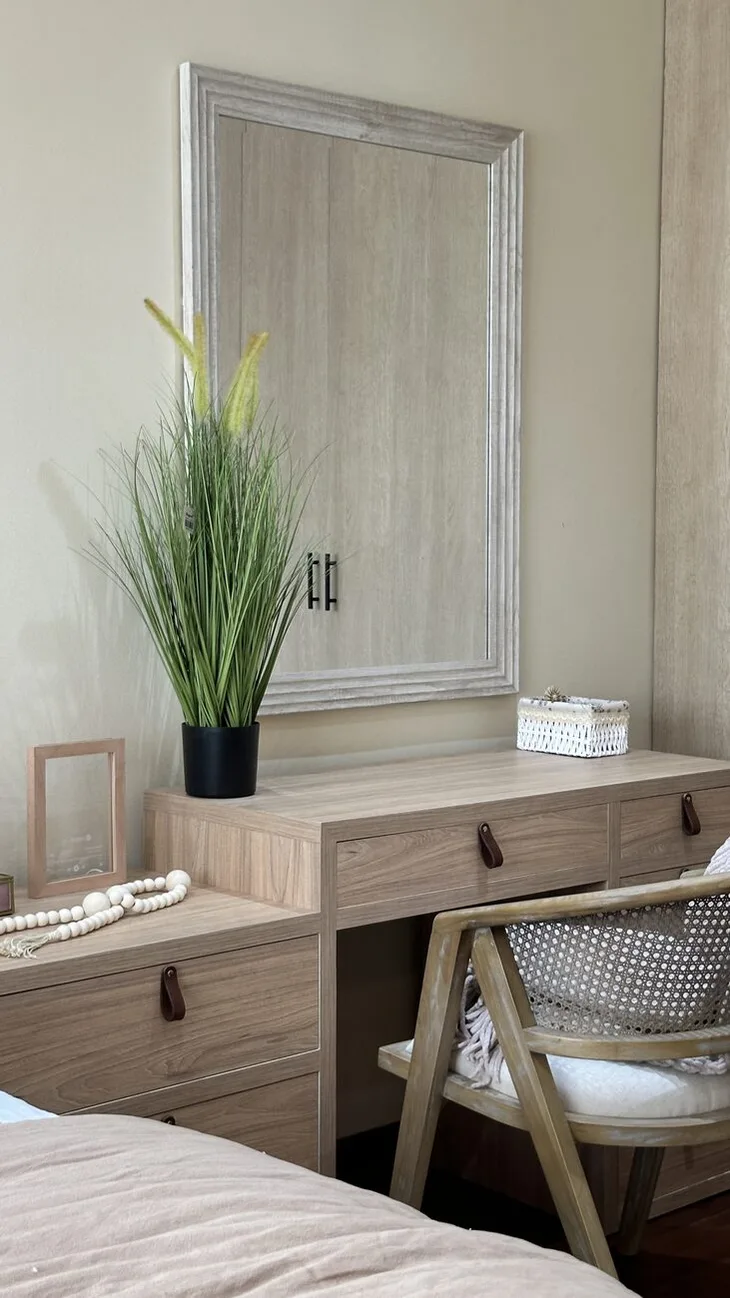 Tocador de madera clara con cajones de tirador de cuero, espejo de marco de madera y una silla de rejilla