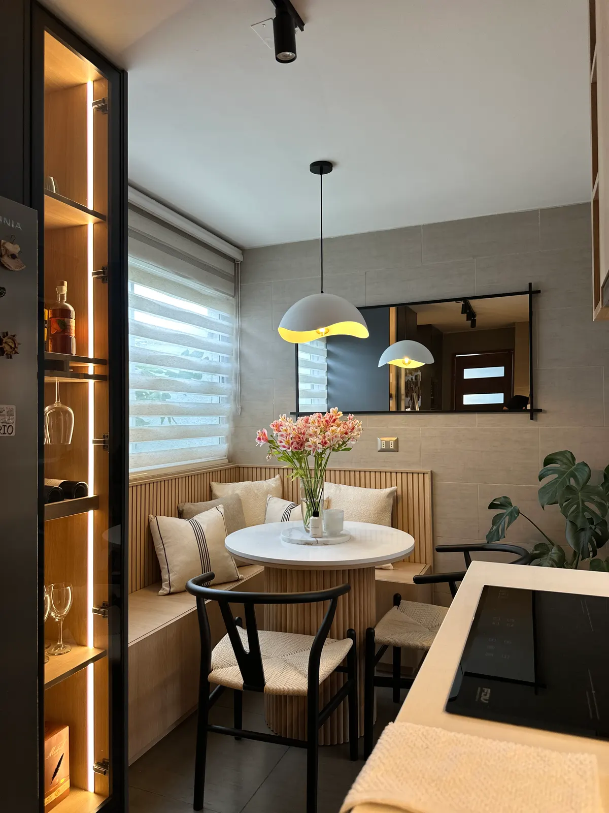 Rincón de comedor con vitrina alta iluminada y banca junto a la ventana