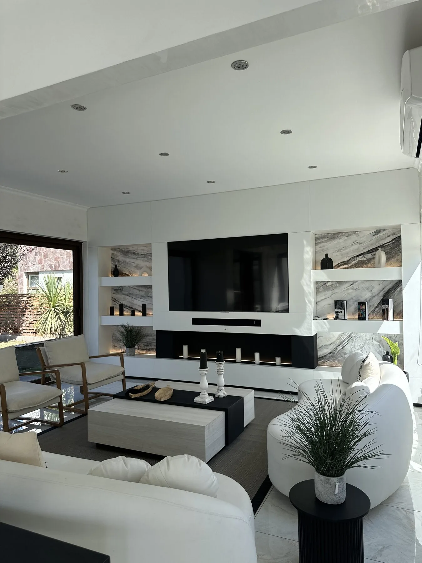 Mueble de living blanco de pared a pared con televisión, chimenea integrada y nichos de fondo veteado