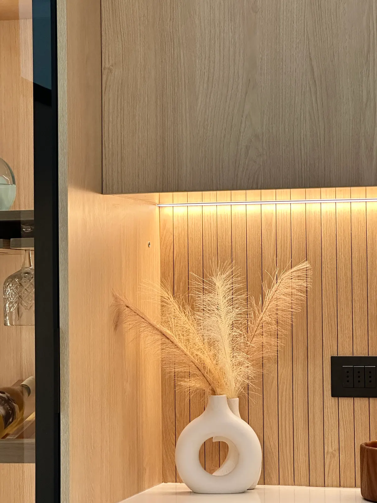 Nicho de roble ranurado con luz cálida y un florero de pampas