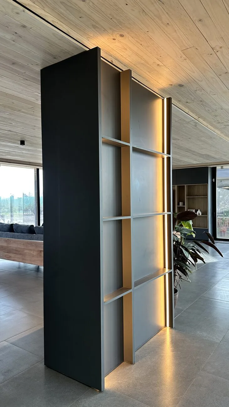 Mueble divisor de piso a cielo, ciego por una cara y con repisas por la otra, con una línea de luz en el canto